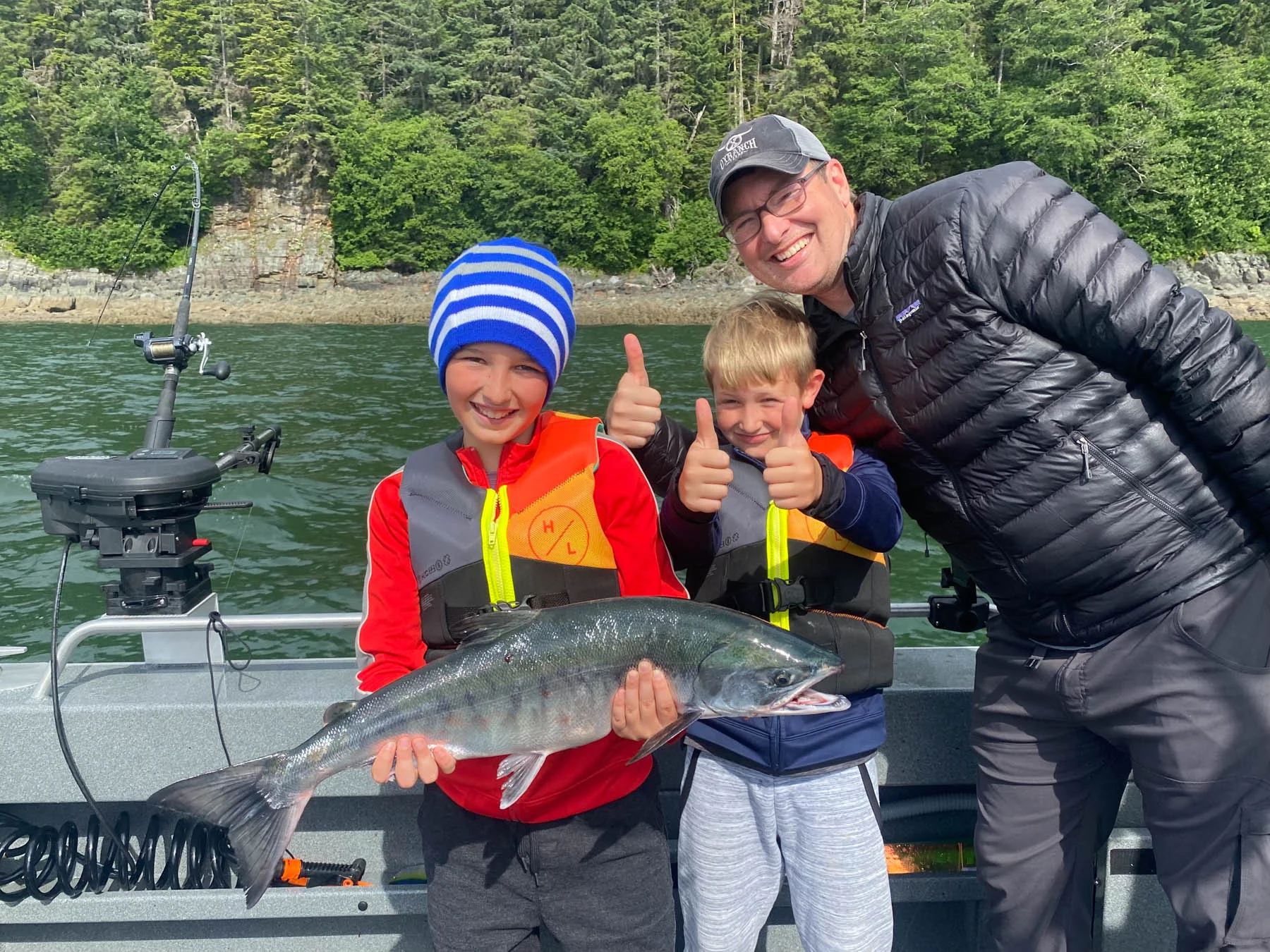 Family on a private fishing charter in Juneau Alaska holding halibut and salmon while whale watching in the background